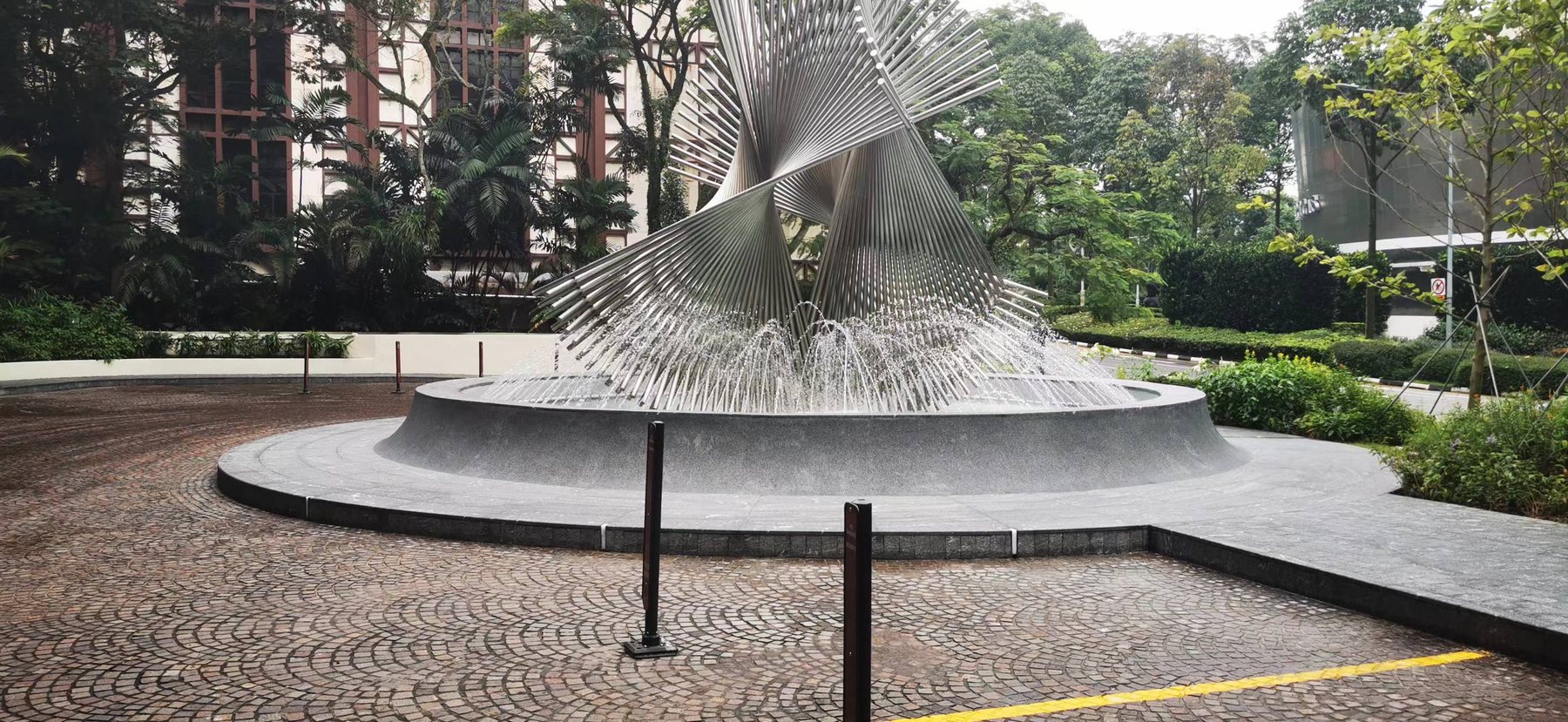 NHB No.13 — Concentric Ring Fountain Paving & Pool Coping Completed circular hotel fountain clad in black Nero Novalato granite, with concentric ring paving and curved pool coping around a polished steel water sculpture
